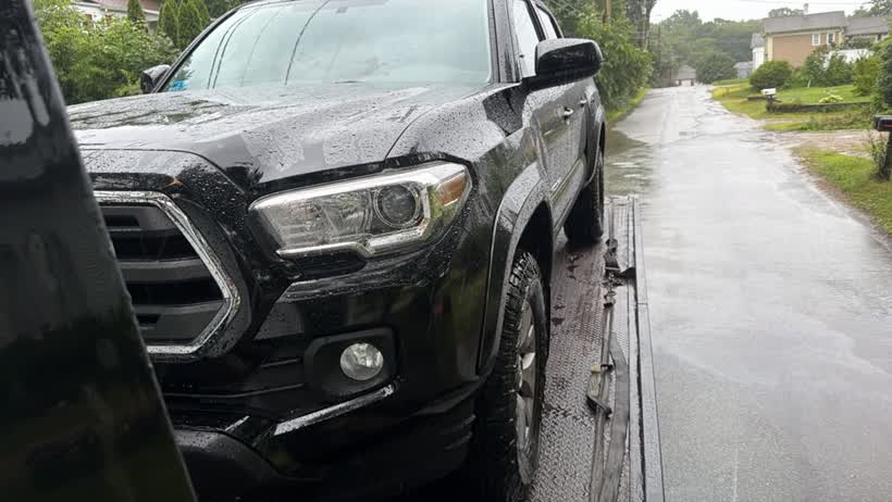 Black pickup loaded on the flatbed on a wet road