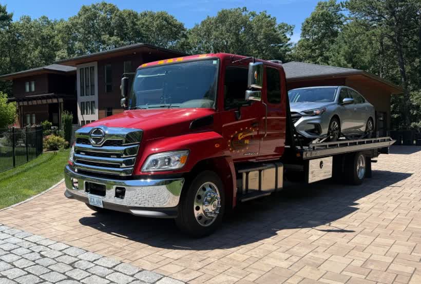 The red Centri Auto flatbed with a car loaded outside a house